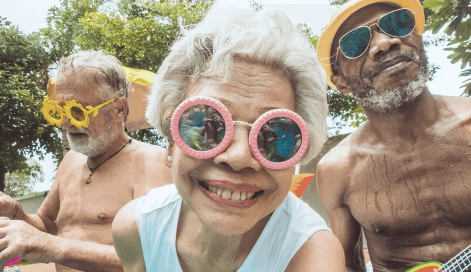 close-up of a senior lady with sunglassess smiling with two elderly men behind her