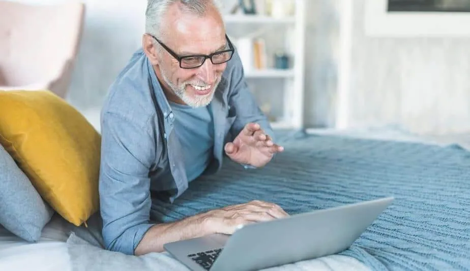 senior man laughing on the bed in front of a laptop