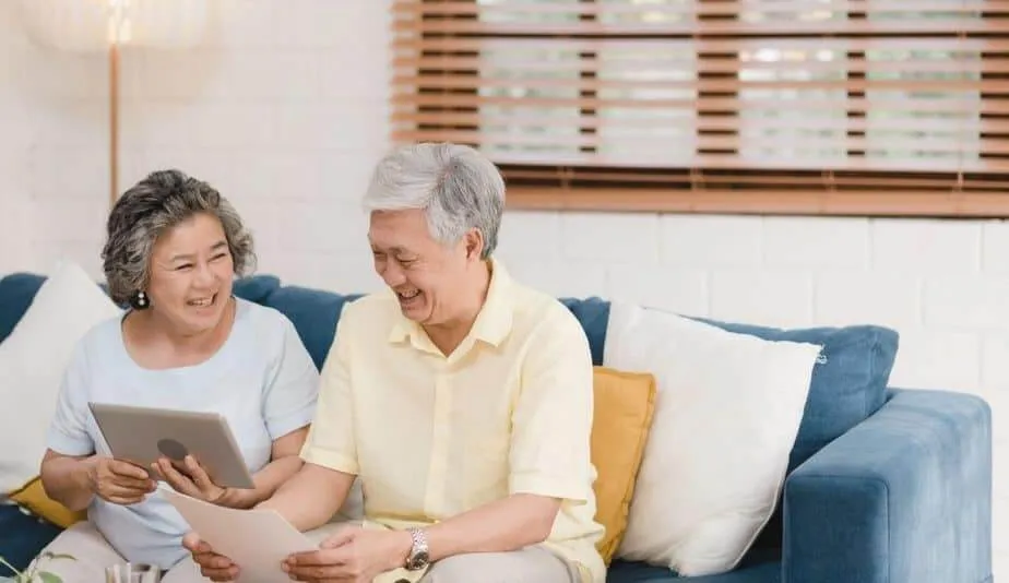 senior couple looking at a tablet and laughing while sitting on a blue couch