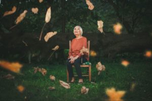 senior woman sitting in a chair in nature looking at leaves falling down