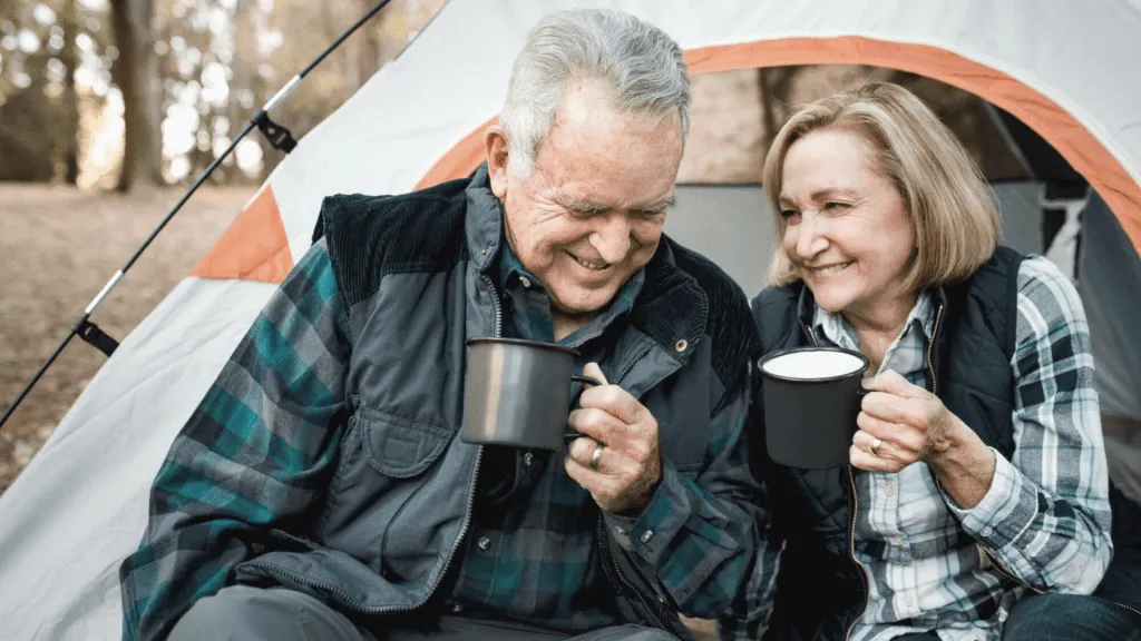 retired senior couple camping, drinking from cups, and laughing