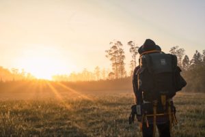 man with hiking gear looking at the sunset on a meadow