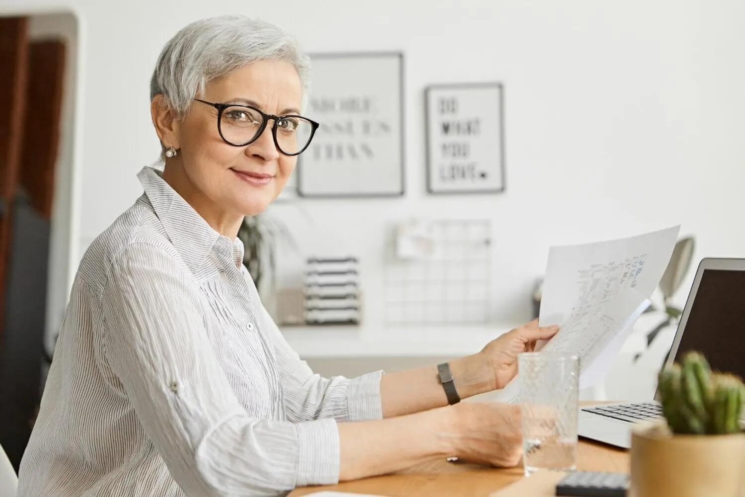 beautiful-successful-confident-mature-businesswoman-with-short-gray-hair-working-her-office-using-portable-computer-holding-papers-her-hands-studying-financial-report-smiling
