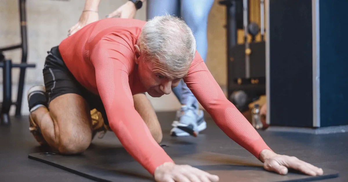 senior man performing stretches on a mat in the gym