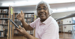 senior black man with headphones holding a thumbs up in a library
