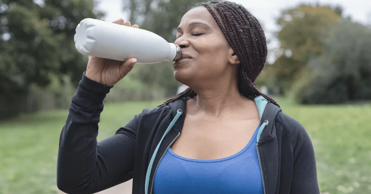 older woman drinking water out of a reusable bottle in a park