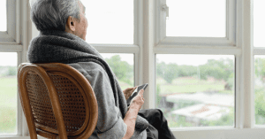 lonely senior man sitting on a chair in front of the window