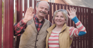 senior parents waving goodbye in front of a wooden fence
