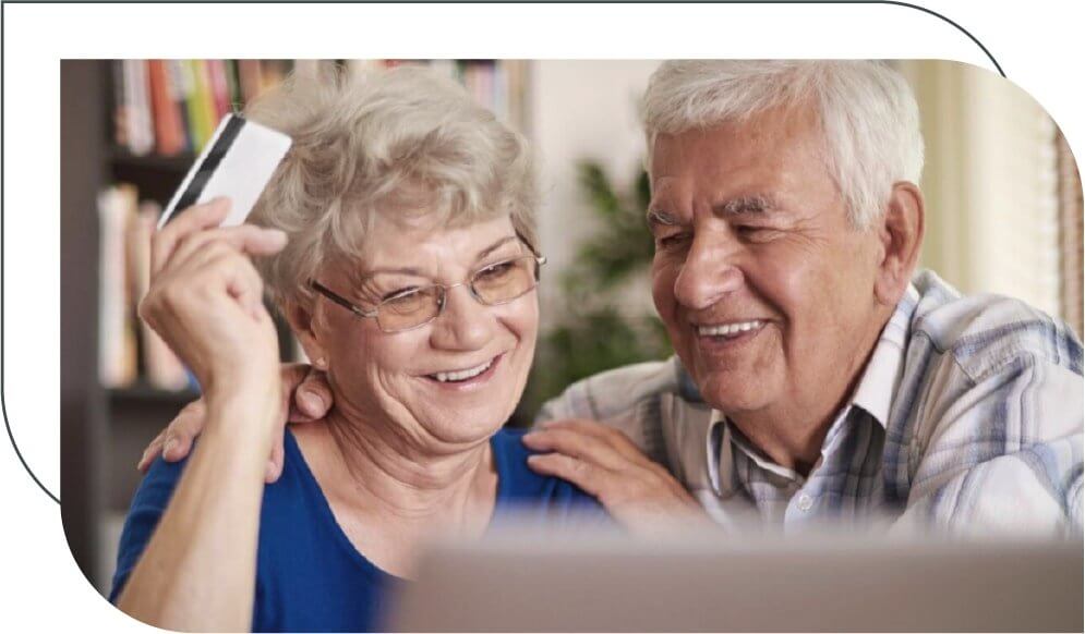 senior couple laughing in front of a laptop holding a credit card