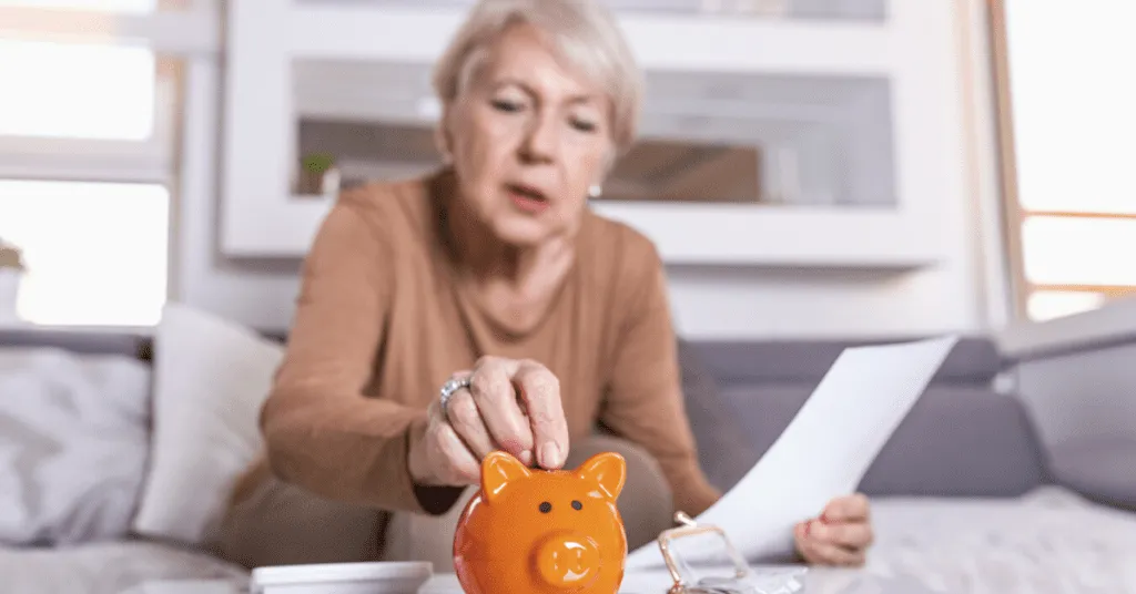 senior woman looking at her finances and putting coins in an orange piggy bank