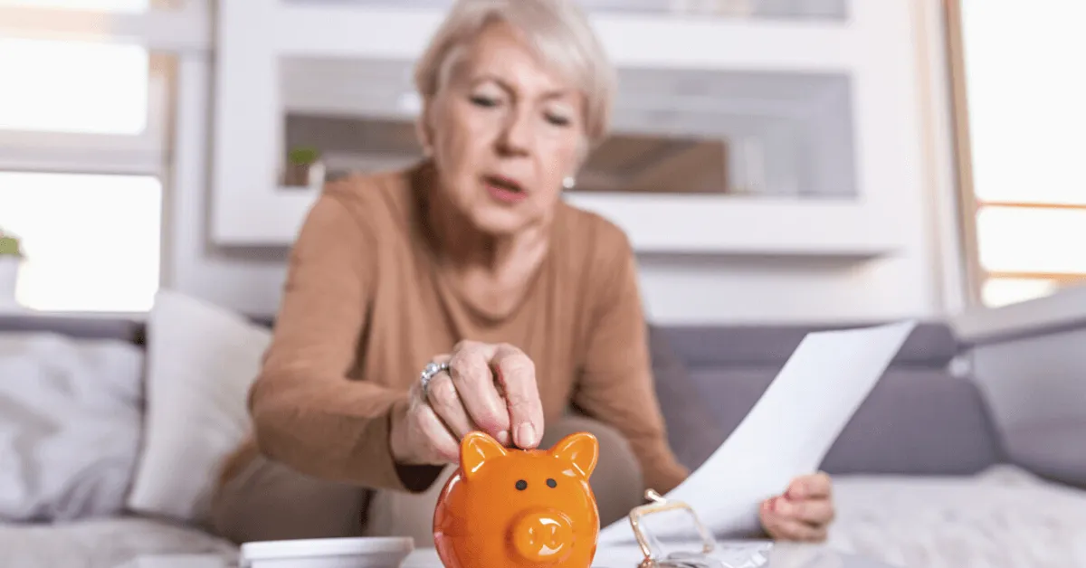 senior woman looking at her finances and putting coins in an orange piggy bank