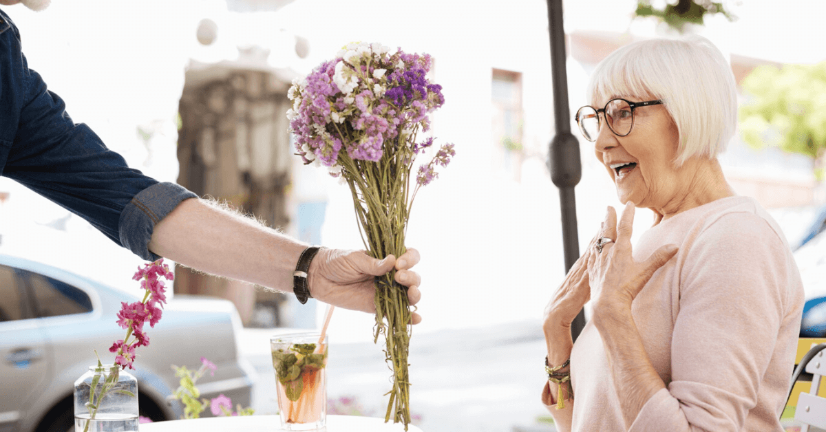 suprised senior woman receiving flowers in a cafe