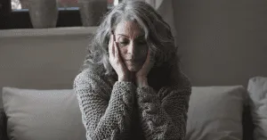 older sad and worried woman sitting on a couch cupping her face