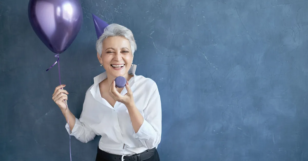 senior retired woman celebrating with a balloon and a party hat