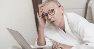 exhausted senior woman sitting on the bed with a laptop