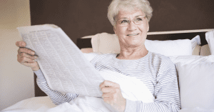 senior woman with glasses reading the newspaper in bed